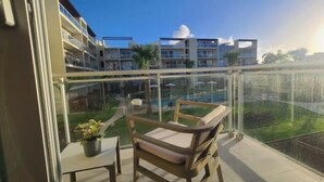 A balcony with a wooden chair and table, overlooking a pool and a building complex. - vr207h+c. Lovely apartment with pool view.

 (Bayahibe)