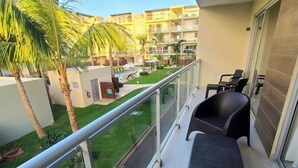 A balcony with wicker furniture, a pool, and a view of a building with multiple balconies and palm trees. - Fantastic view of the pool vr222 h+c
 (Bayahibe)
