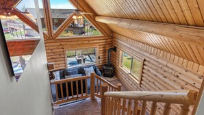L’intérieur d’une cabane en rondins comprend une chambre à coucher située en mezzanine, une cheminée et un balcon avec des sièges d’extérieur.