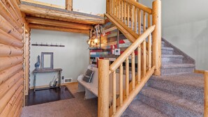 Un escalier en bois avec une rampe, une petite table sur laquelle se trouvent un vase et un miroir, et un mur équipé d’un panneau perforé.