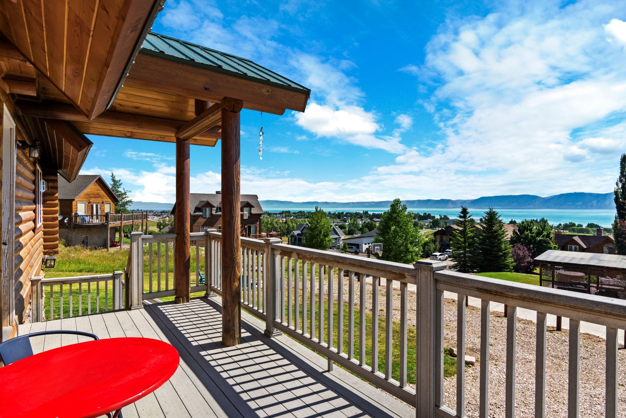 Une terrasse en bois avec une table rouge, offrant une vue sur un lac et des montagnes.