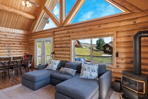 Ein Holzblockhaus-Interieur mit einem Ecksofa, einem Esstisch, Stühlen und einem Kamin.