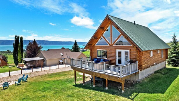 Une cabane en rondins dotée d’une terrasse, d’un espace salon extérieur couvert et offrant une vue sur un lac.