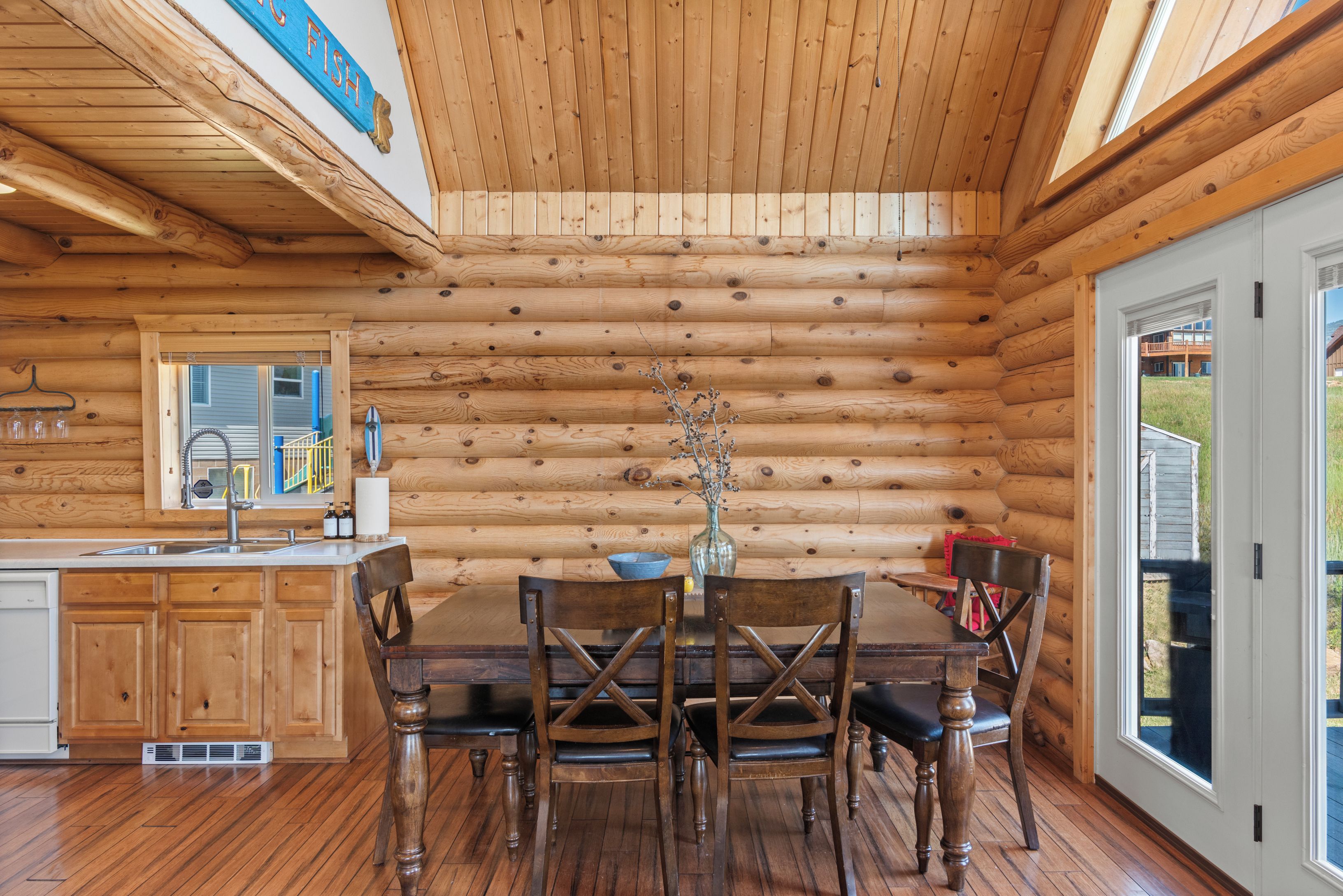 Interno di una baita di legno con zona pranzo, pareti in legno e vista attraverso una porta vetrata.
