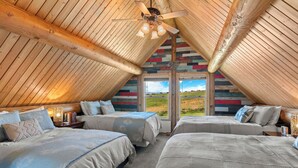 Une chambre confortable, avec un toit en bois, deux lits, un ventilateur de plafond et une grande fenêtre donnant sur l’extérieur.