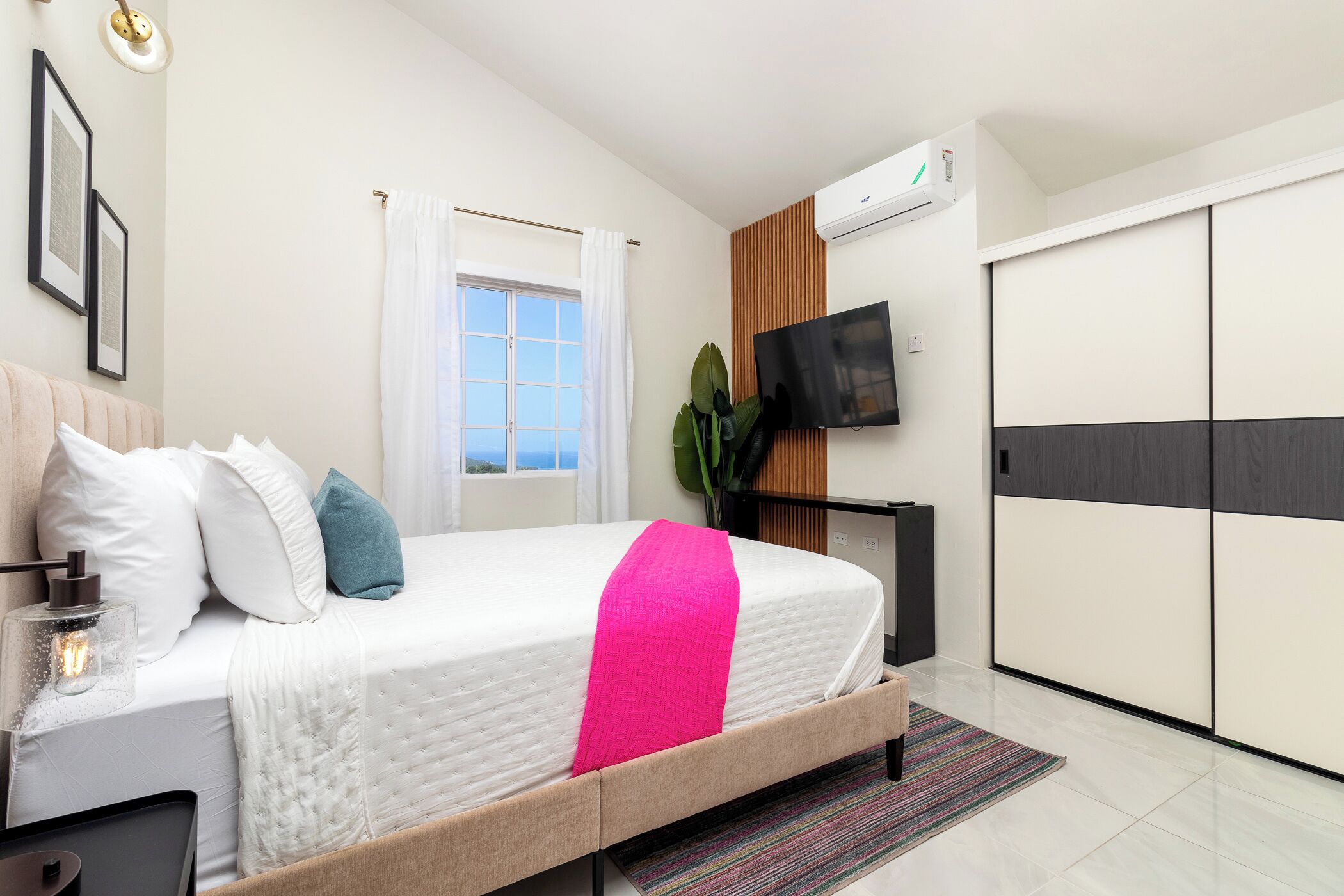 Moderni hotellihuone, jossa on sänky, televisio, vaatekaappi ja ikkuna, jossa on verhot.