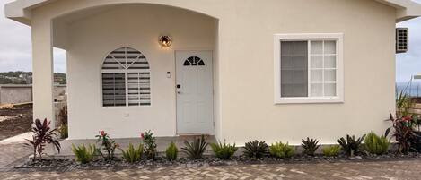 A single-story house with a white facade, a front door, a window, and a small porch area.