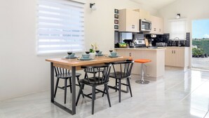 A modern kitchen with a dining area, featuring a wooden table, black chairs, and a view of the outdoors. - Sunset at ArecaHomes~ Beach Access~ Pool & Water Park (Discovery Bay)