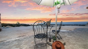 A patio with two metal chairs, a table, a hat, and a bottle under a white umbrella. - Sunset at ArecaHomes~ Beach Access~ Pool & Water Park (Discovery Bay)