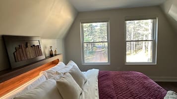 A bedroom with a bed, two windows, a headboard, and a view of trees.