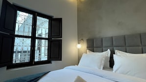 Un dormitorio con cama, almohadas, una ventana con vistas y una lámpara de pared.