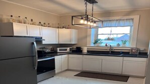 Una cocina con armarios blancos, un refrigerador de acero inoxidable, un microondas y una ventana con plantas.
