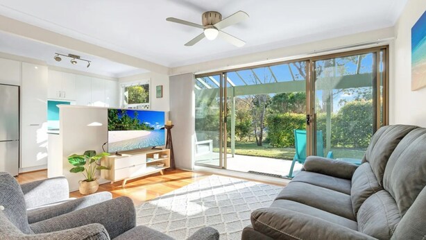 Una sala de estar moderna con un televisor de pantalla plana grande, un ventilador de techo y un puertas correderas de vidrio que dan a un jardín.