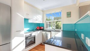 Cocina moderna con armarios blancos, encimera negra y ventana con vistas a zonas verdes.