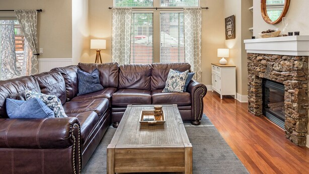 A spacious living room with a large leather sectional sofa, a wooden coffee table, and a stone fireplace. - Serenity Awaits: Pine Trees Retreat w/ AC and EV (Flagstaff)