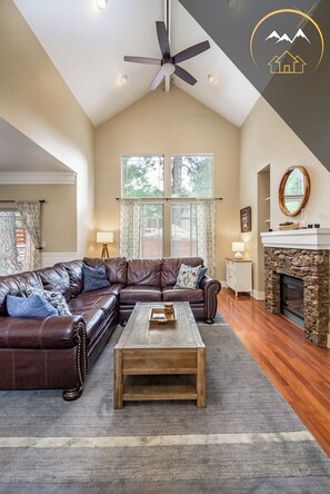 A spacious living room with a large leather sectional sofa, a wooden coffee table, and a stone fireplace. - Serenity Awaits: Pine Trees Retreat w/ AC and EV (Flagstaff)