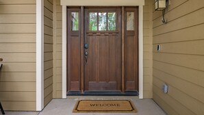 A wooden front door with a 'WELCOME' mat, a mailbox, and a wall-mounted light fixture. - Serenity Awaits: Pine Trees Retreat w/ AC and EV (Flagstaff)