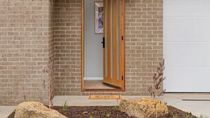 A brick building with a wooden door, a garage door, and a small garden with rocks and plants. - Central Studio in new townhouse! (Beechworth)