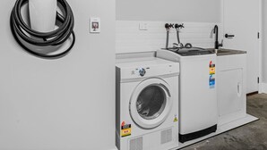 A laundry room with a washing machine and dryer, a coiled power cord, and a door. - Central Studio in new townhouse! (Beechworth)