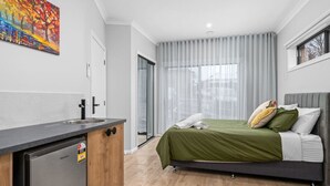 A modern bedroom with a bed, a small kitchenette, and a sliding glass door to a balcony. - Central Studio in new townhouse! (Beechworth)
