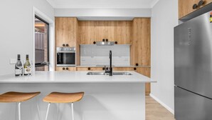 A modern kitchen with a central island, stainless steel appliances, wooden cabinets, and bar stools. - New Central 2 bedroom townhouse! (Beechworth)
