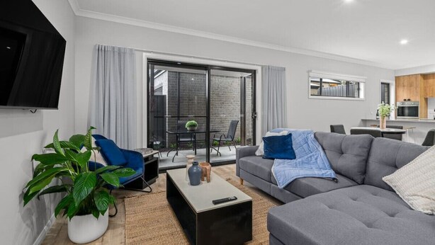 A modern living room with a grey sofa, a blue armchair, a coffee table, and a TV mounted on the wall. - New Central 2 bedroom townhouse! (Beechworth)