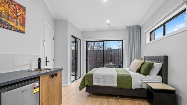 A modern bedroom with a bed, bedside table, and a view of the outdoors.