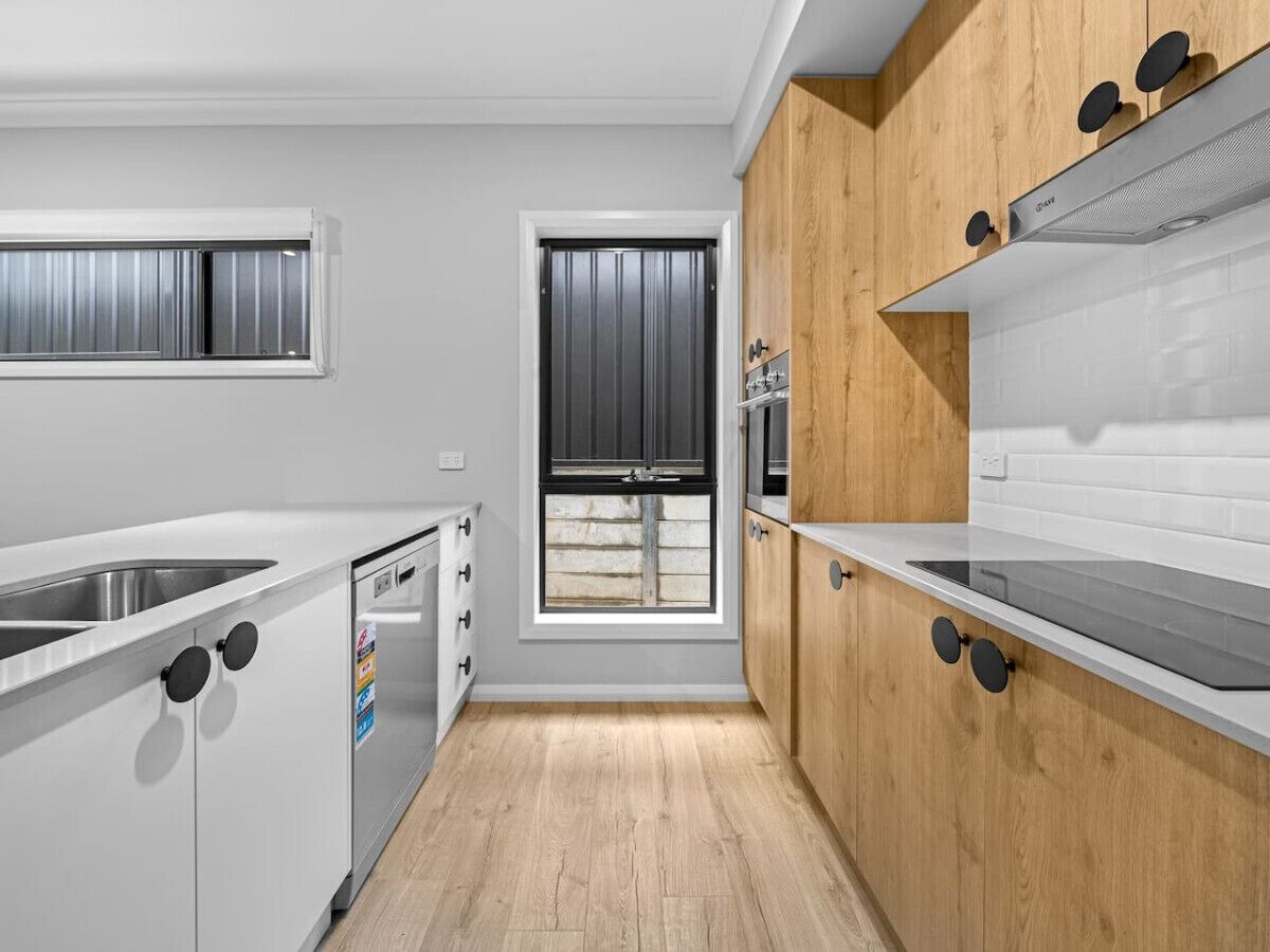 Een moderne keuken met witte kastjes, een raam en een ingebouwde kookplaat.