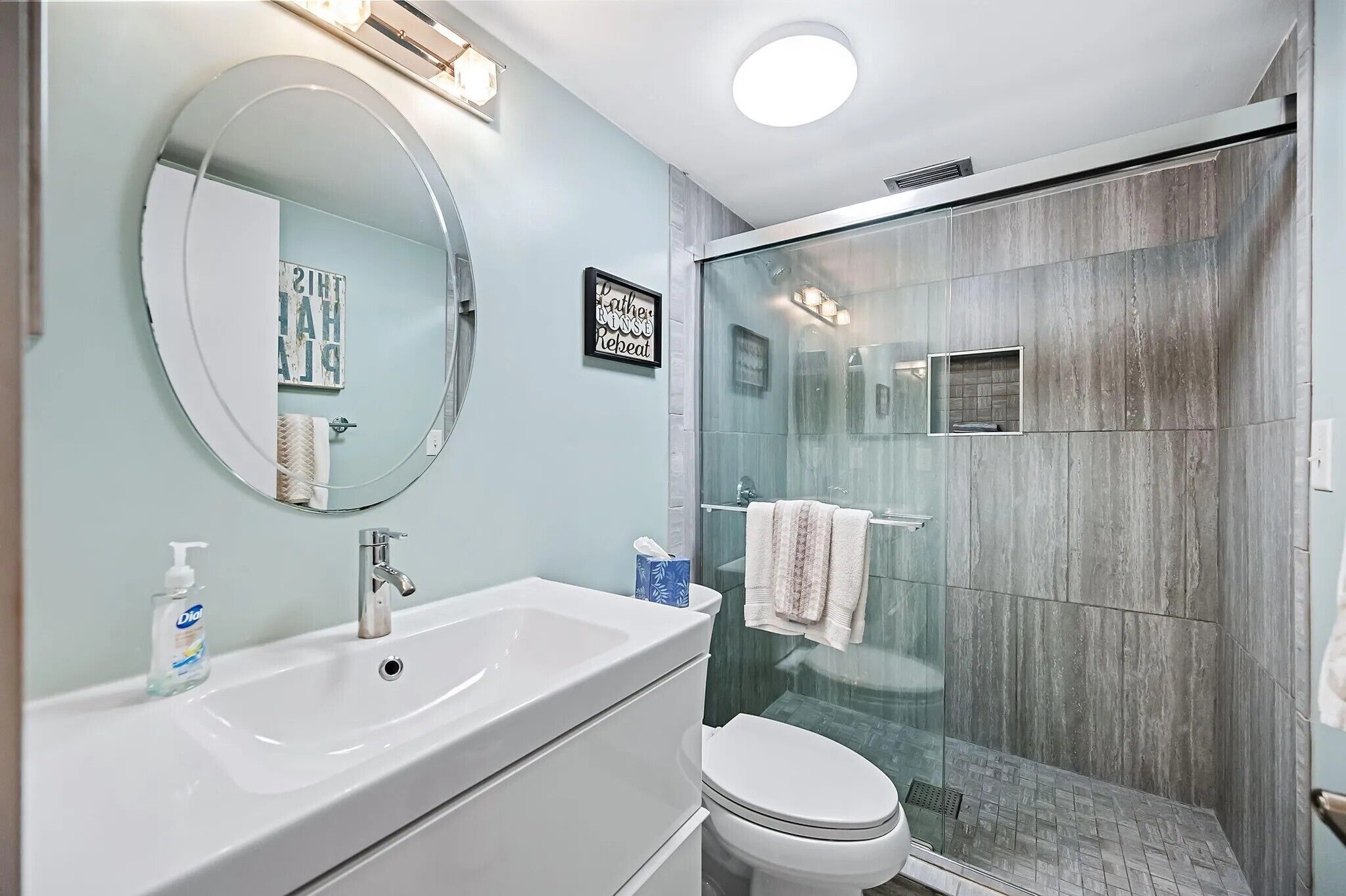 Une salle de bain moderne avec un grand miroir, un lavabo et une douche à parois de verre.