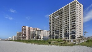A beachfront hotel with multiple high-rise buildings, a sandy beach, and a wooden walkway leading to the beach. - Beachfront paradise in this gorgeous renovated ground floor condo! (Marco Island)