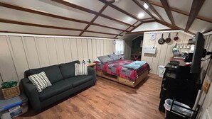 Habitació petita amb sofà, llit, sòl de fusta i zona de cuina equipada.