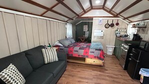 Habitació senzilla amb llit, sofà, petita cuina i terra de fusta.