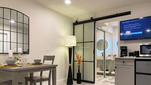 A modern kitchen with a flat-screen TV, a coffee machine, and a sliding glass door leading to a dining area. - Luxury, Private Suite 2 (Palm Beach Gardens)