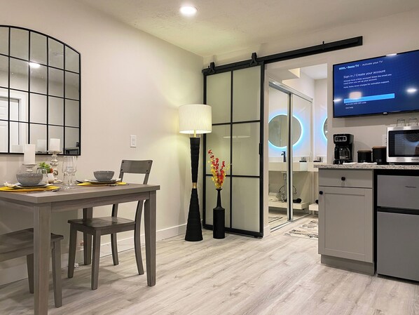 A modern kitchen with a flat-screen TV, a coffee machine, and a sliding glass door leading to a dining area. - Luxury, Private Suite 2 (Palm Beach Gardens)