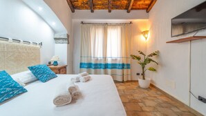 A bedroom with a bed, towels, a potted plant, a TV, and a window with curtains. - PV9: One-Bedroom Apartment with Romantic Terrace in the City Center (Olbia)
