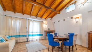 A living room with a wooden ceiling, a dining area with blue chairs, and a fireplace. - PV9: One-Bedroom Apartment with Romantic Terrace in the City Center (Olbia)