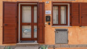 A building with a stone facade, two wooden doors with glass panels, and a small window with shutters. - PV9: One-Bedroom Apartment with Romantic Terrace in the City Center (Olbia)