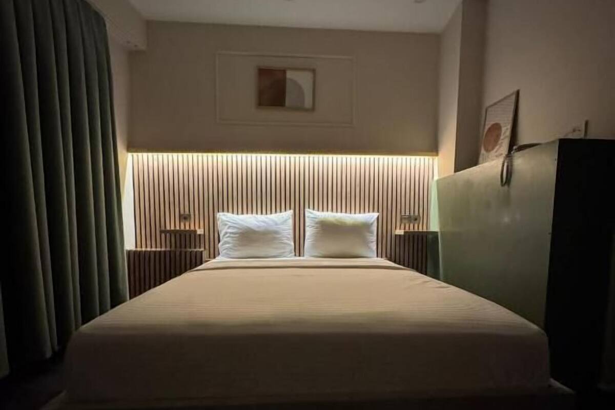 A hotel room with a large bed, a headboard with vertical lines, a small picture on the wall, and a nightstand with a lamp.