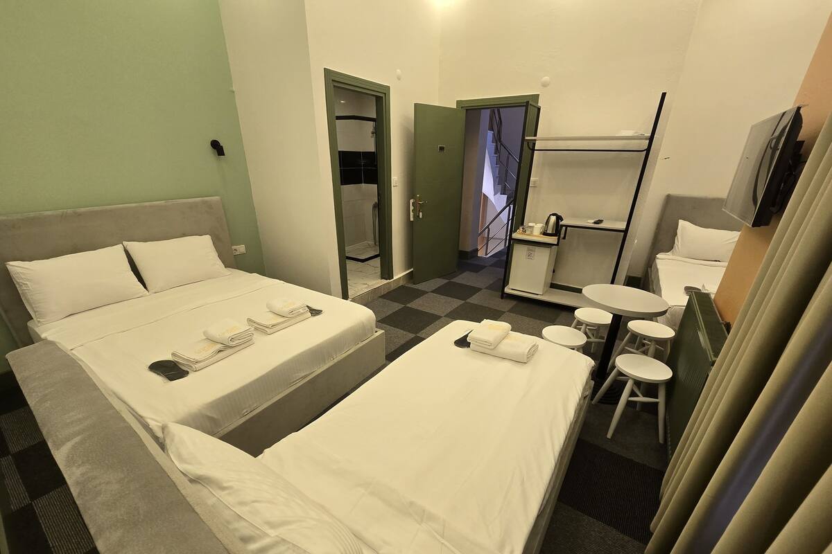 A hotel room with two beds, a small desk, a chair, a mirror, and a TV.