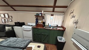 Ein kleines Zimmer mit Bett, Küchenzeile und einer Wand, an der ein Schild mit dem Schriftzug 'Good Things' befestigt ist.