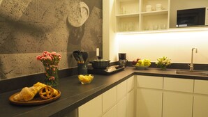 Een keuken met een donker aanrecht, witte kastjes, een koffiezetapparaat, een schaal fruit en een bloemenvaas.