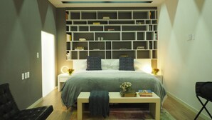 Een moderne slaapkamer met een groot bed, nachtkastjes, een boekenkast, en een klein tafeltje met boeken en bloemen.