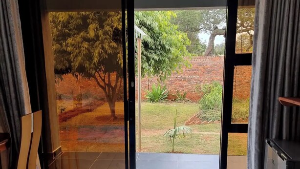 A room with a large sliding glass door leading to a garden with trees and a brick wall.