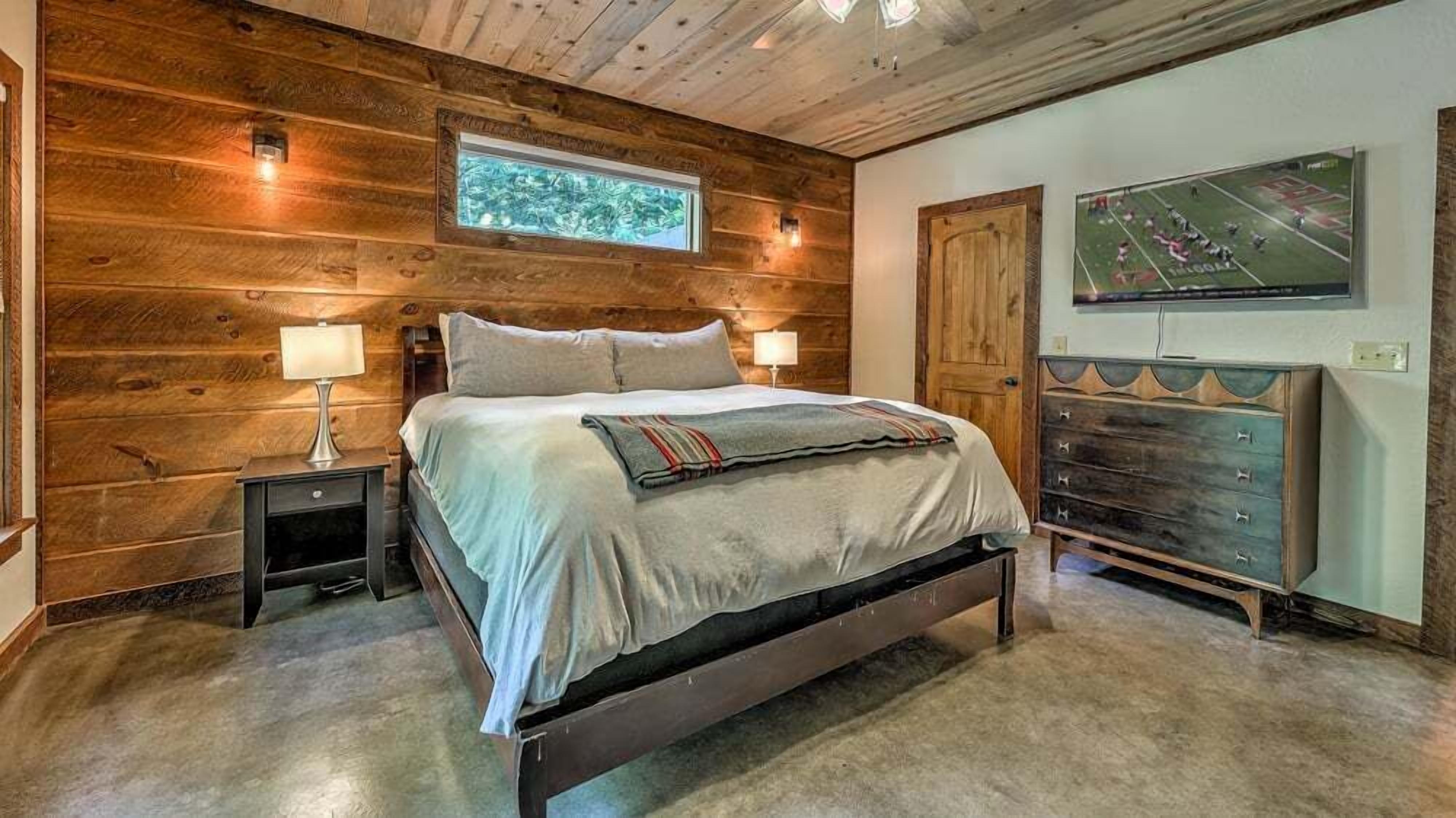 A wooden-paneled bedroom with a bed, nightstands, a dresser, and a TV mounted on the wall.