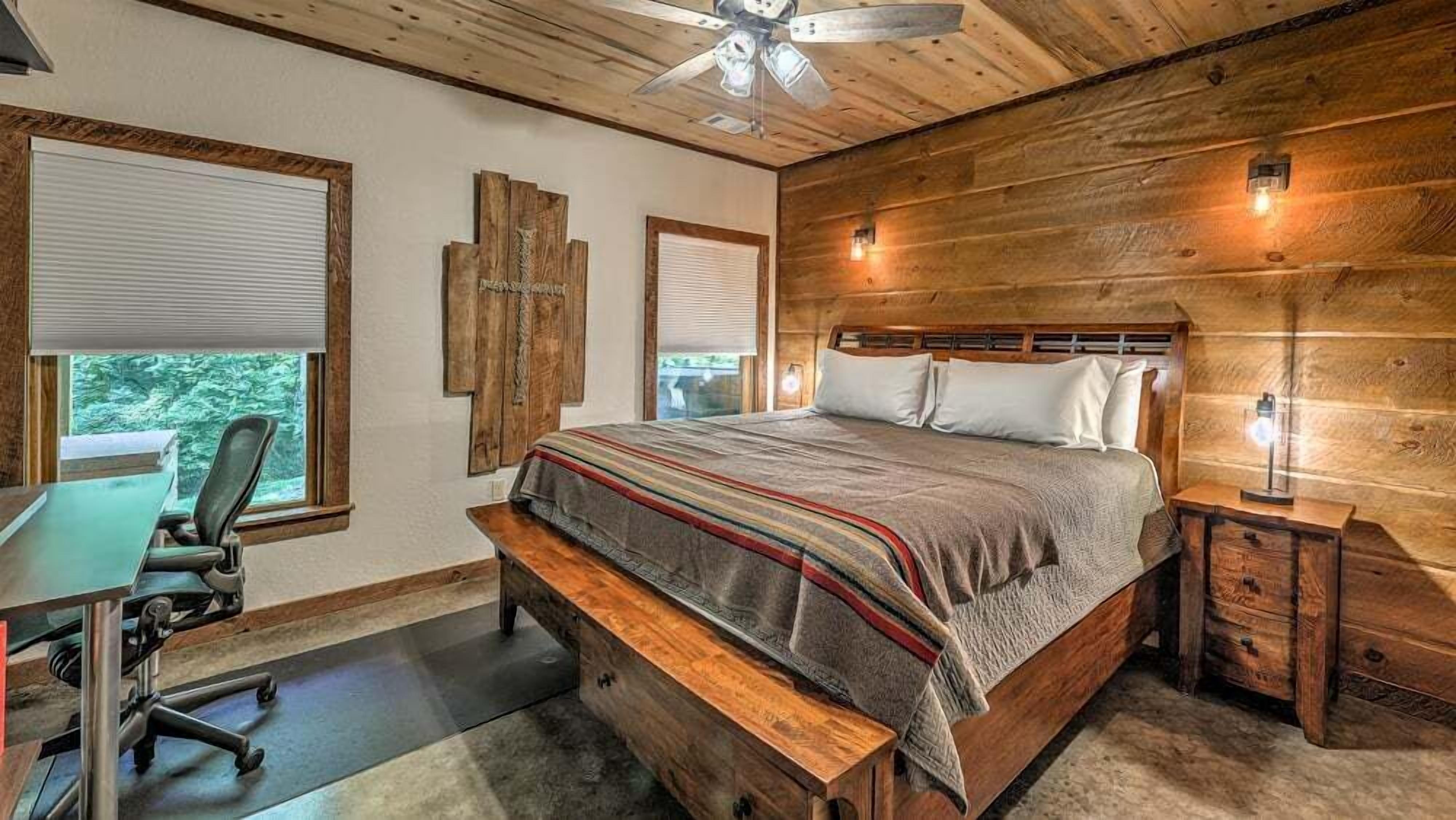 Un dormitorio con cabecera de madera, cama grande, escritorio con silla y vista al exterior a través de una ventana.