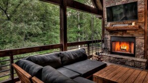 Un área de estar acogedora al aire libre con chimenea de piedra y televisor en la pared.