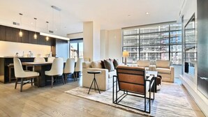 A modern living room with a dining area, large windows, and a kitchen.