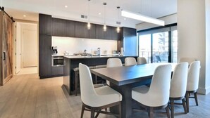 A modern kitchen with dark cabinetry, a central island, and a dining area with six chairs.