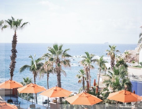 A poolside area with orange umbrellas, palm trees, and a view of the ocean.