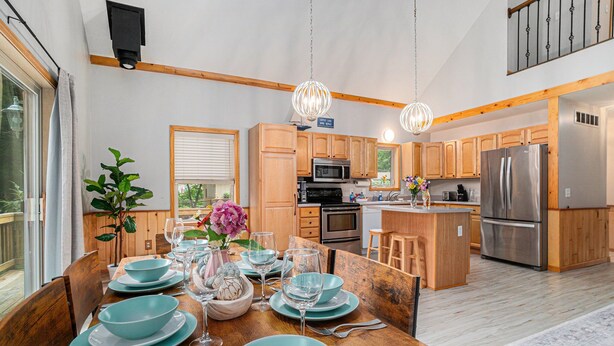 Una cocina moderna con armarios de madera, electrodomésticos de acero inoxidable y un comedor listo para seis personas, con platos y copas azules.